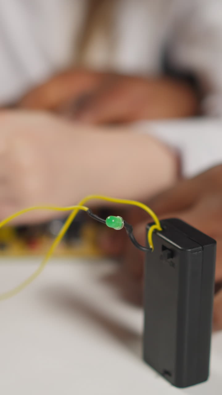 Little girl takes probes from chip to turn off green lamp with African-American physics teacher at table in science school laboratory close view