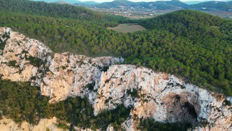 Hikers-rest-on-a-rocky-cliff-among-trees-with-a-view-of-the-green-landscape-during-sunset-in-ibiza