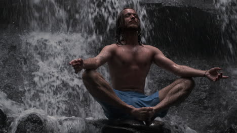 young man meditating under waterfall.