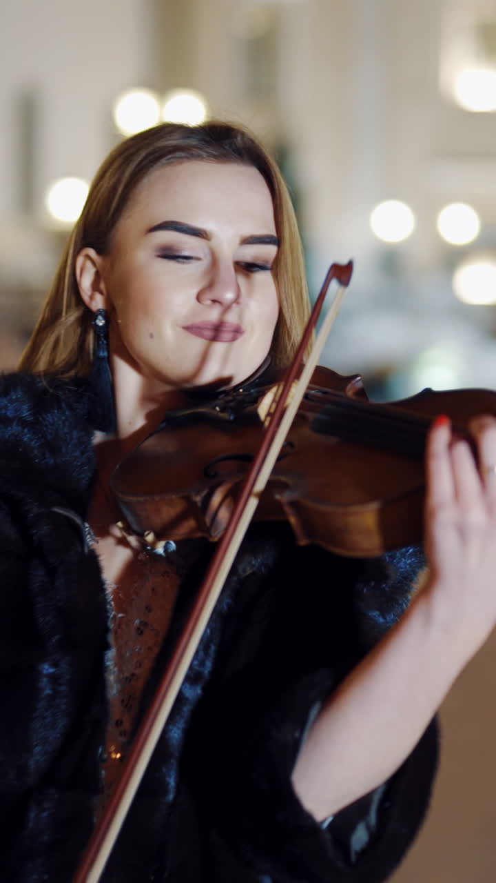 Young lady playing the violin on the street. Violinist playing in the middle of the street with luxury background. Vertical video
