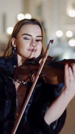 young lady playing the violin on the street. violinist playing in the middle of the street with luxury background. vertical video