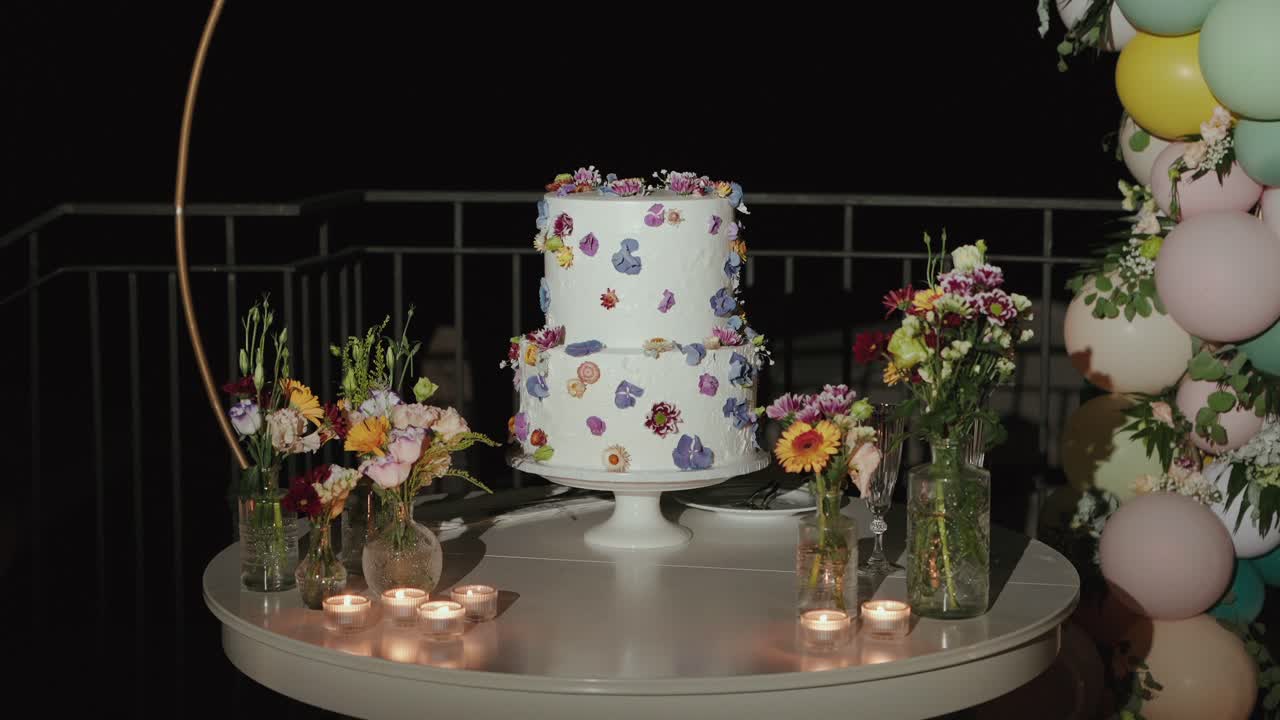 Tarta nupcial con adornos florales rodeada de velas y globos