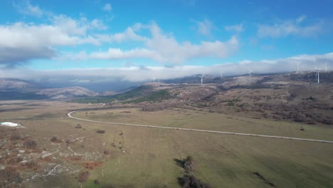 Beautiful-aerial-shot-of-Croatian-landscape-with-wind-turbines-generating-renewable-energy-in-the-background-and-an-empty-road,-in-the-region-of-Lika-in-Croatia,-Europe