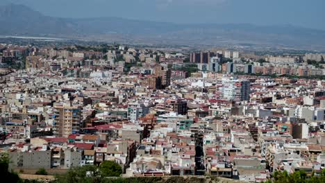 a panoramic landscape of a vast city highlights a mix of old and modern buildings, with a majestic mountain range serving as a scenic backdrop of alicante city in spain.