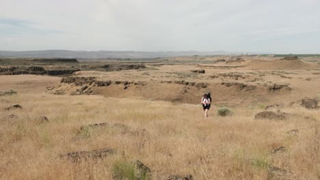 woman with tripod in backpack hikes arid grassland of wa scablands