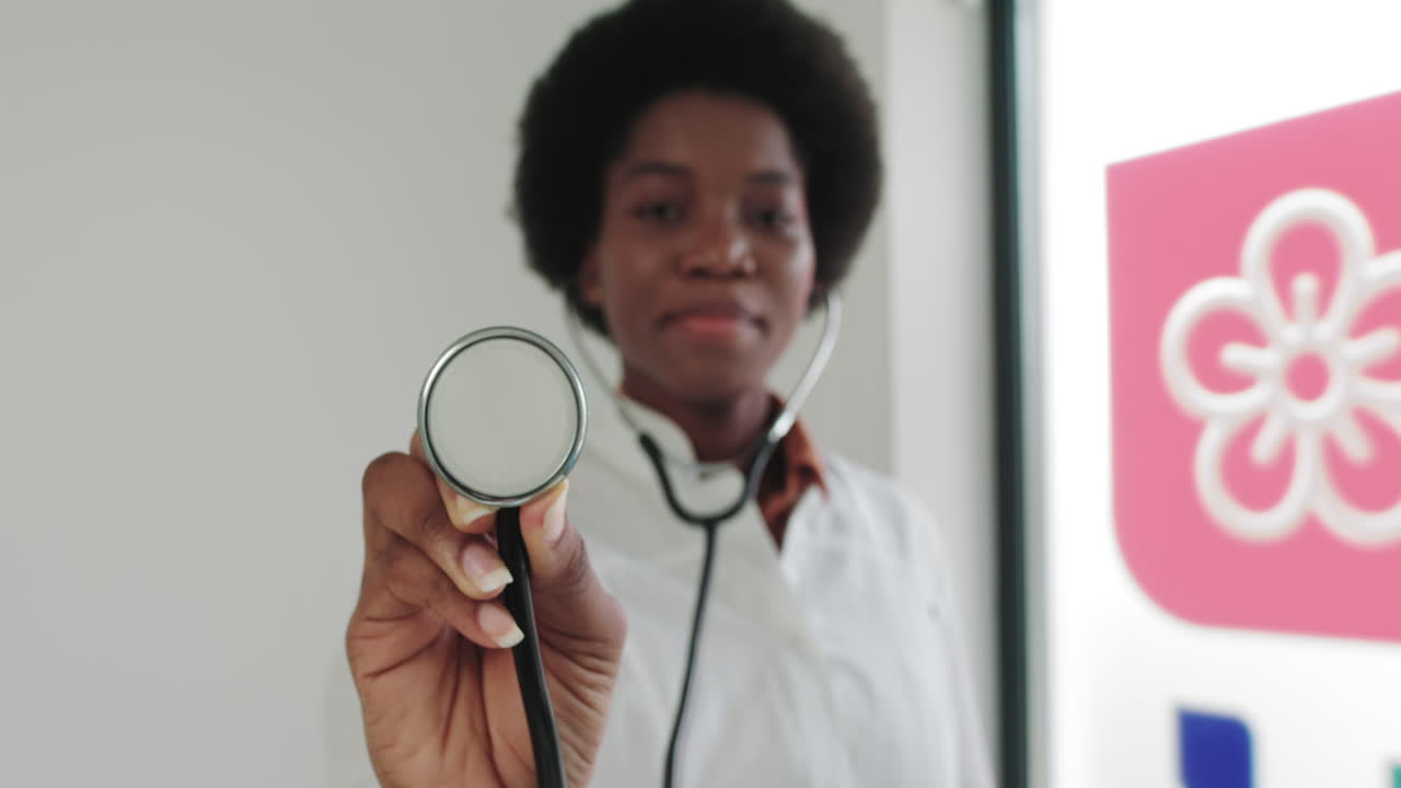 Primo piano di una dottoressa con stetoscopio che visita una donna afroamericana in camice bianco in una clinica