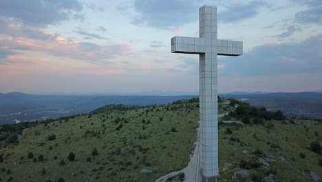 blue light aerial ascends up christian millennium cross on grassy hill