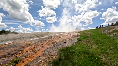 tourists visiting the upper geyser basin trail in yellowstone national park, wyoming, usa. liquid run off streaming down the hillside.