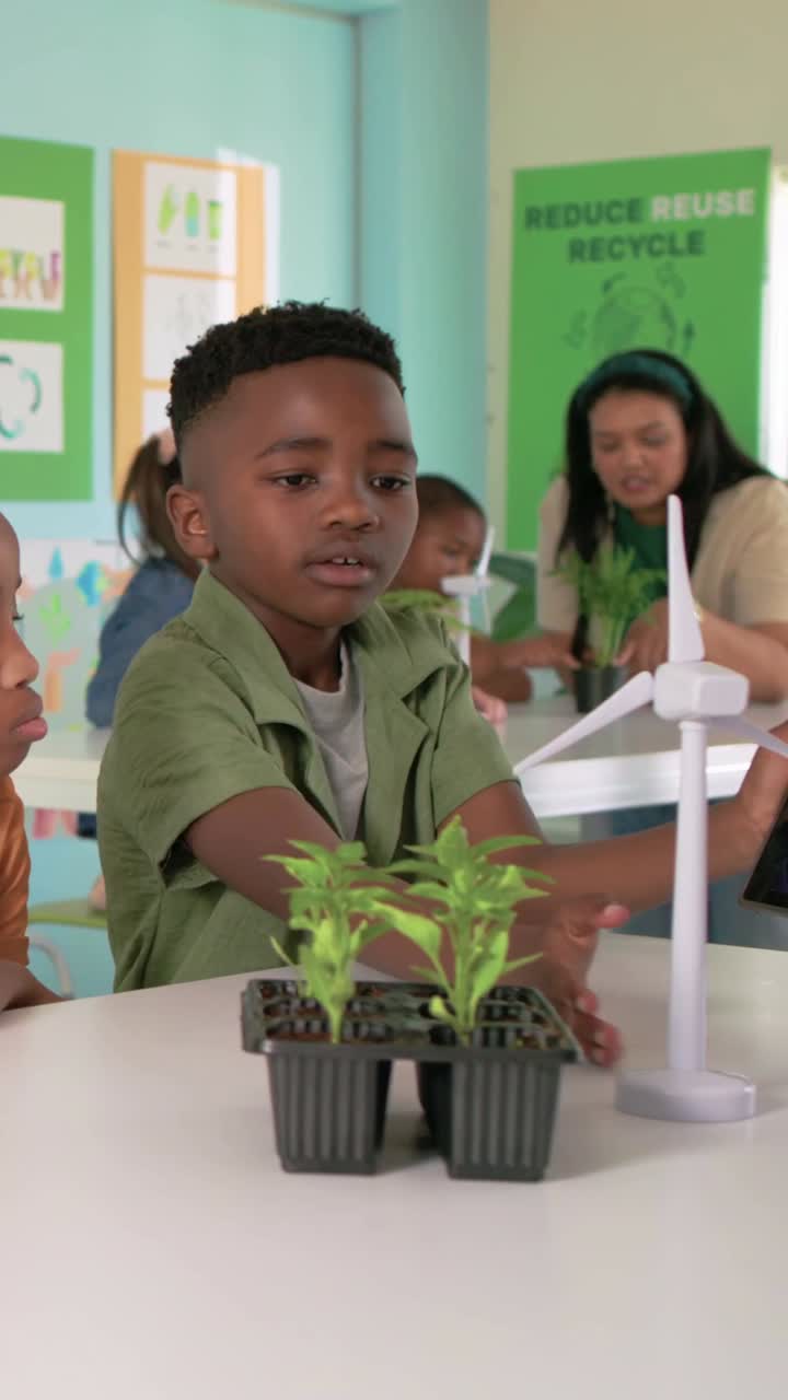 Vertical video: Adjusting tablet, boy in green top spinning blades near seedlings in class for STEM