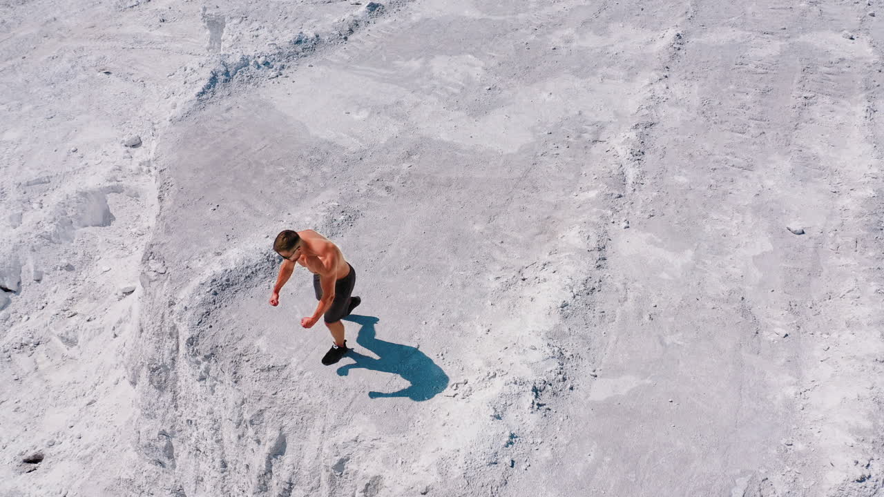 Muscular man on the edge of white hill. Shirtless sportsman shows his strong body on the rocky canyon on the natural summer background. Drone view.