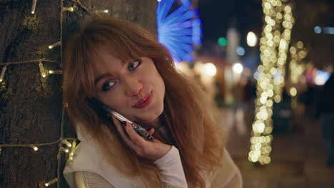 smiling woman talking smartphone on festive street closeup. lady in luna park