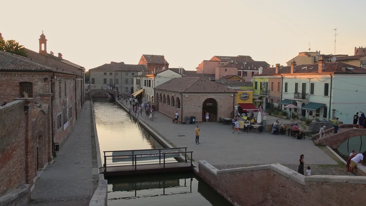 Comacchio, Italian old town with canal, bridge, people walking at golden sunset