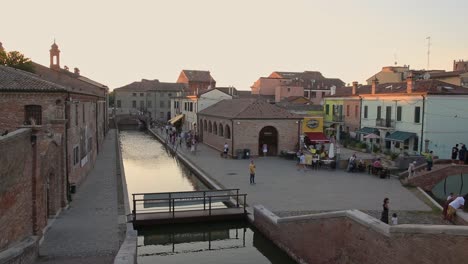 comacchio, italian old town with canal, bridge, people walking at golden sunset
