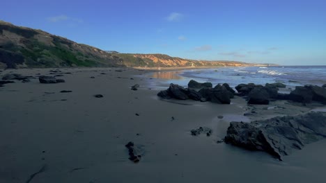 Corona-Del-Mar-Beach-with-a-wide-angle-static-view-of-the-rocks-with-cliffs-and-small-waves-of-the-pacific-ocean-in-the-back