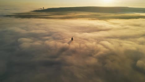 italy matera, drone video orbiting around partially visible tower that protrudes through low hanging clouds during sunrise, golden colours incredible view