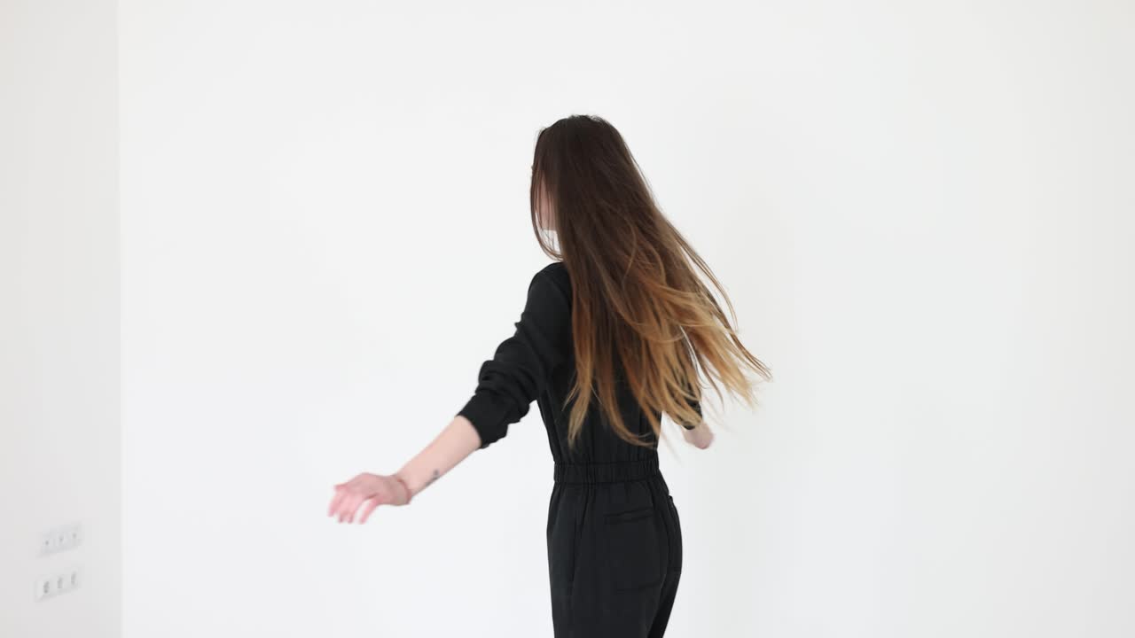 A woman in a black jumpsuit gracefully turns and dances in a white studio
