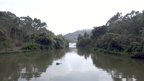 Langsamer-Flug-über-Den-Fluss,-Der-Zum-Stausee-Führt,-Umgeben-Von-Baumlaub