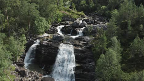 Aerial-slowly-flying-forward-over-waterfalls-rushing-down-hillside-in-evergreen-forest