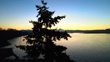 Beautiful-scenery-of-a-sunrise-shot-by-drone-at-a-large-lake-and-trees,-orange-and-blue-sky-coming-together