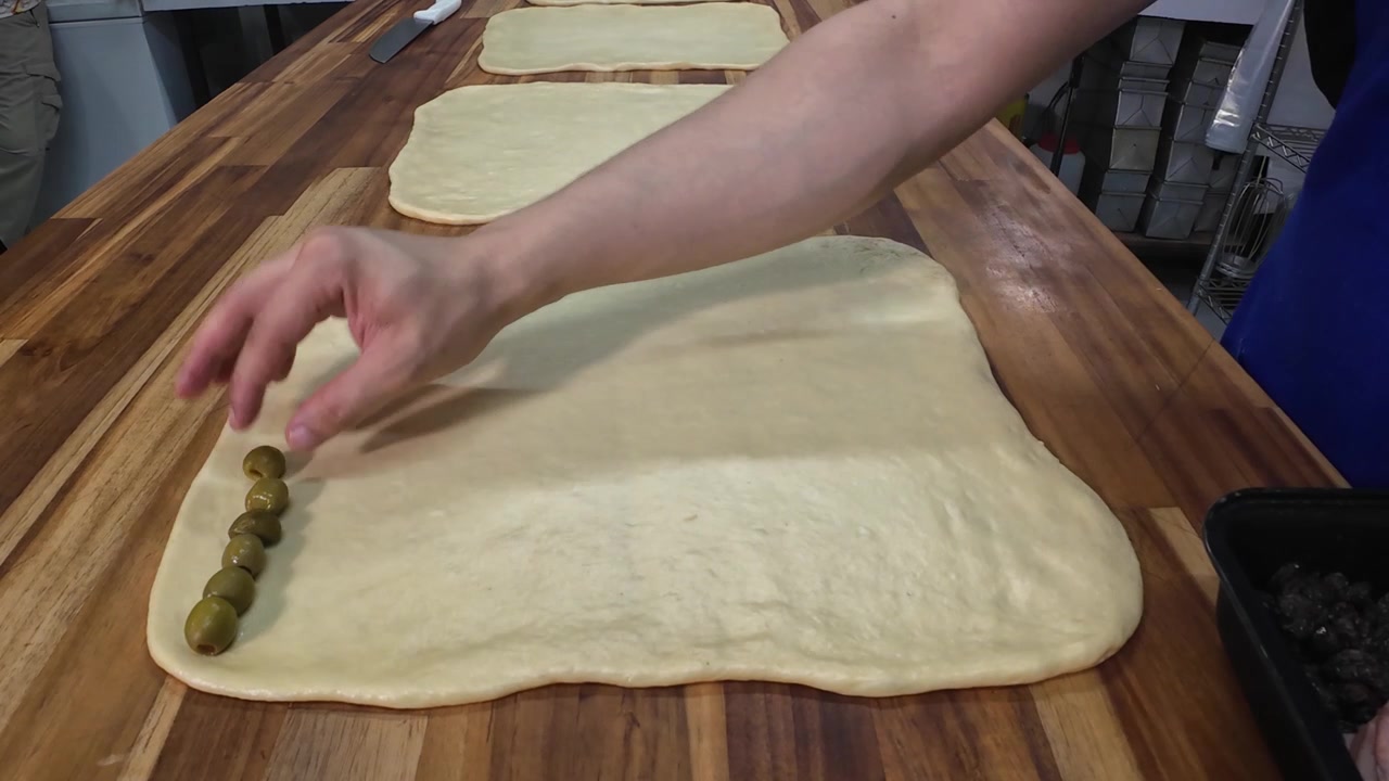 Baker placing green olives on raw dough for ham bread