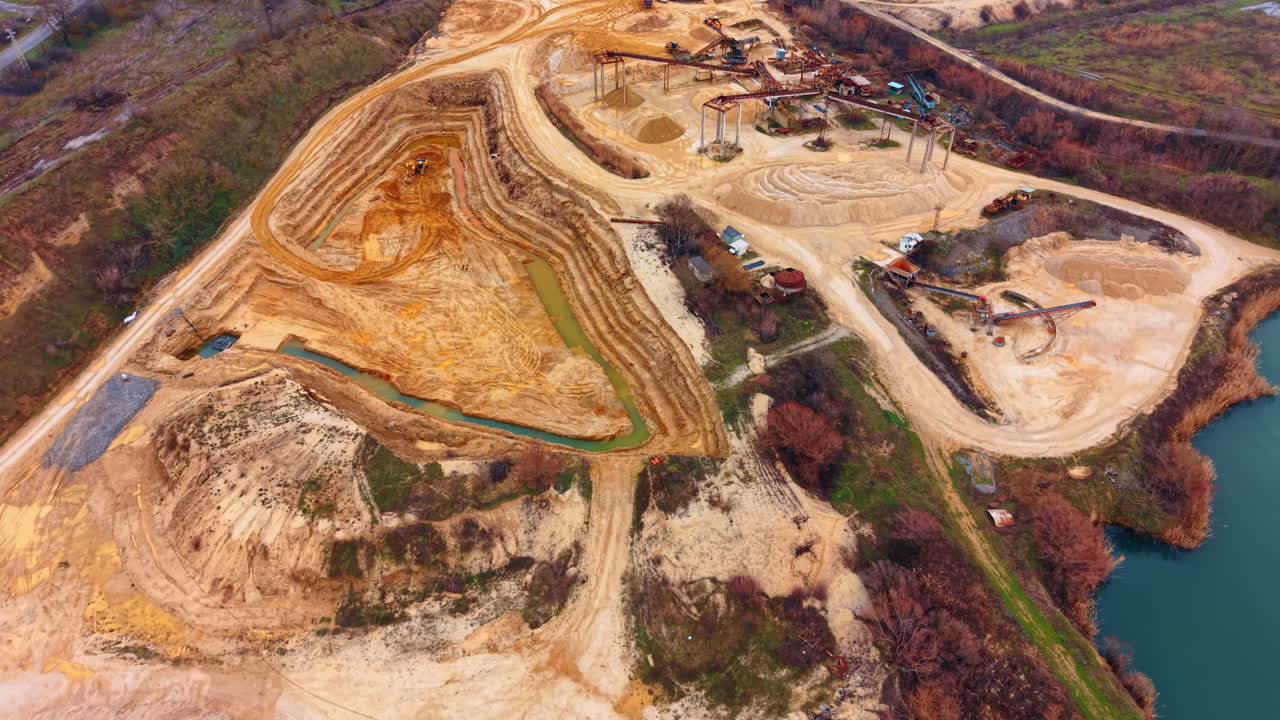 Sand mining site with industrial machinery and artificial lake. High angle view of quarry excavation pit and processing equipment