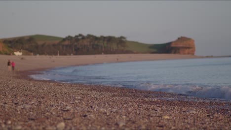 Strandwellen-Schlagen-Auf-Die-Küste,-Menschen-In-Der-Ferne