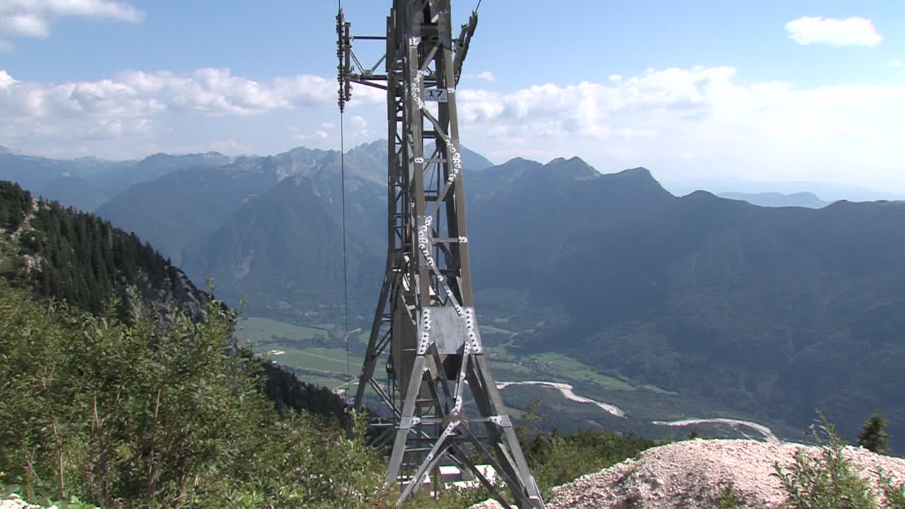 gondola tower above a lush green valley in summer, tilt down, sunny weather