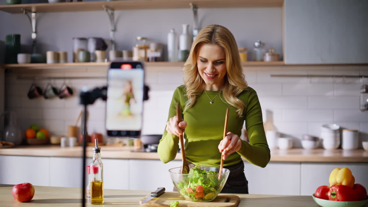 Vlogger de comida demostrando la preparación de ensalada a la cámara del smartphone, primer plano de cocina.