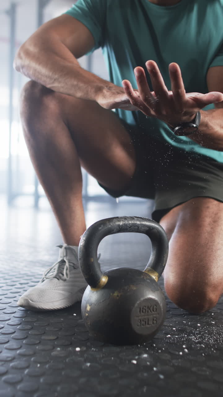 Vertical video: Preparing for workout, man clapping hands with chalk near kettlebell in gym