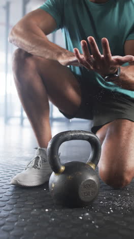 vertical video: preparing for workout, man clapping hands with chalk near kettlebell in gym