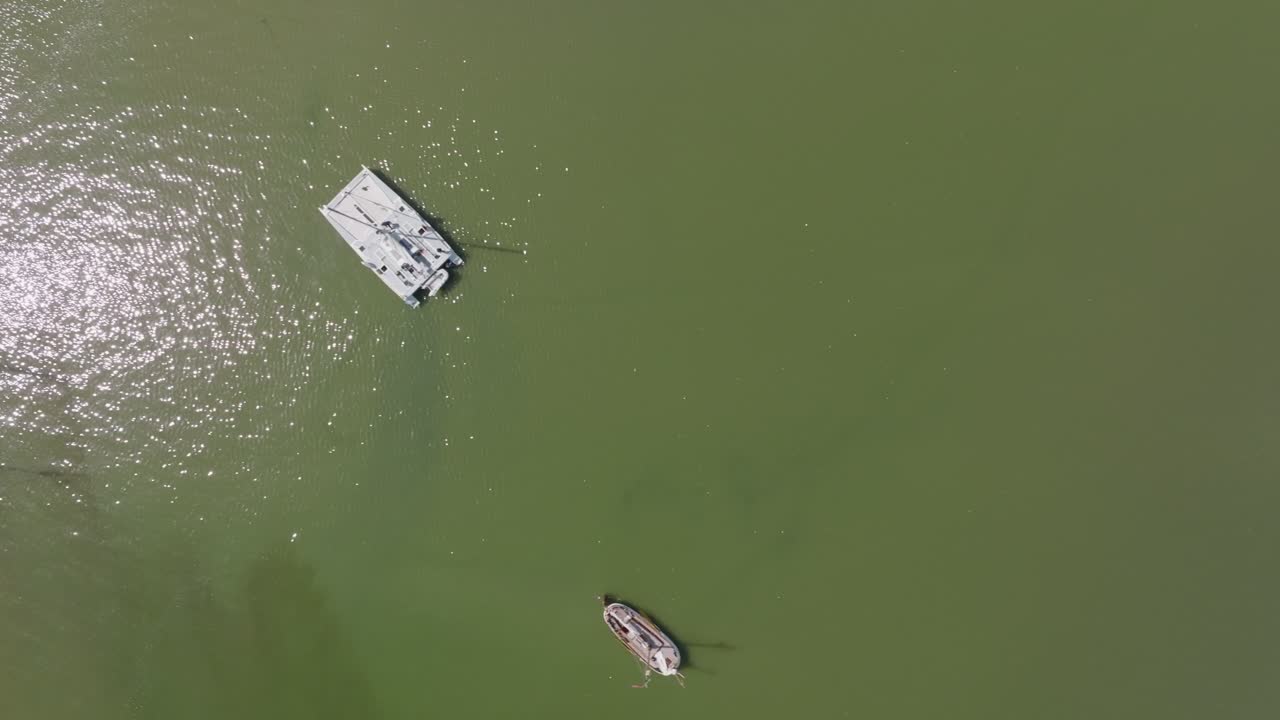Nadir drone view of boats on green open water near tidal flats; top‑down angle, daylight