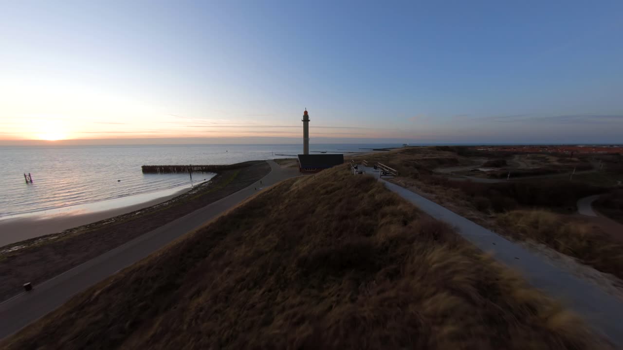 Fast aerial shot going from the sand dunes towards a lighthouse on top of a Dutch dyke