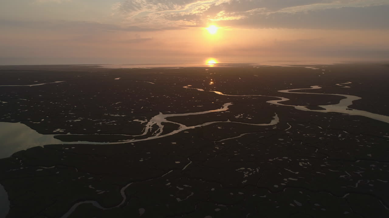 establecimiento de tomas cinematográficas de drones de marisma salada natural y arroyo en marea alta con vías fluviales serpenteantes en el impresionante amanecer naranja en la costa este del norte de norfolk, reino unido