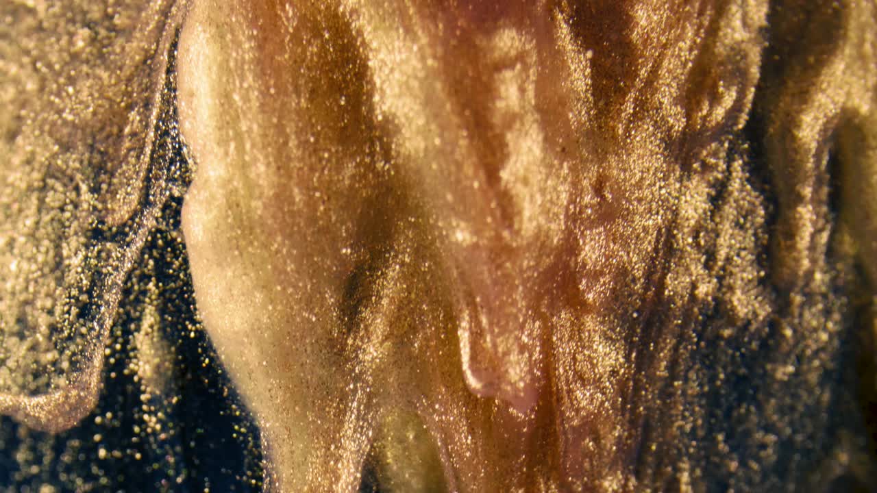 황금 잉크 입자는 검은 바탕에 다채로운 혼란으로 물에 흐른다.