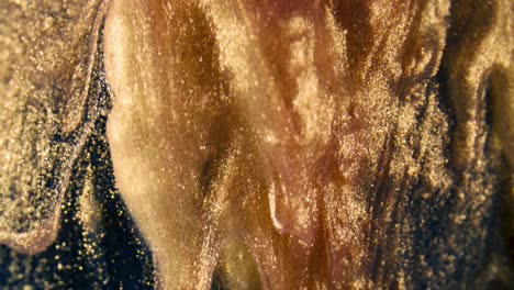 golden ink particles flows in water as colorful chaos on the black background