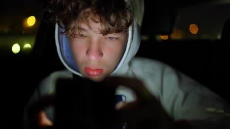 teenage male passenger inside car during nighttime, immersed in smartphone screen, creating soft city lights bokeh in darkened background, capturing contemporary digital lifestyle moment