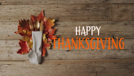 animation of happy thanksgiving text over cutlery and autumn leaves over wooden surface