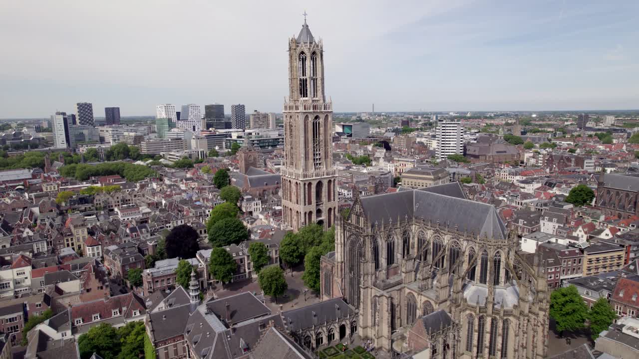 Slow ascending aerial movement showing gothic architecture of cathedral and De Dom church tower in historic city center of Utrecht with Dutch high rise buildings in background