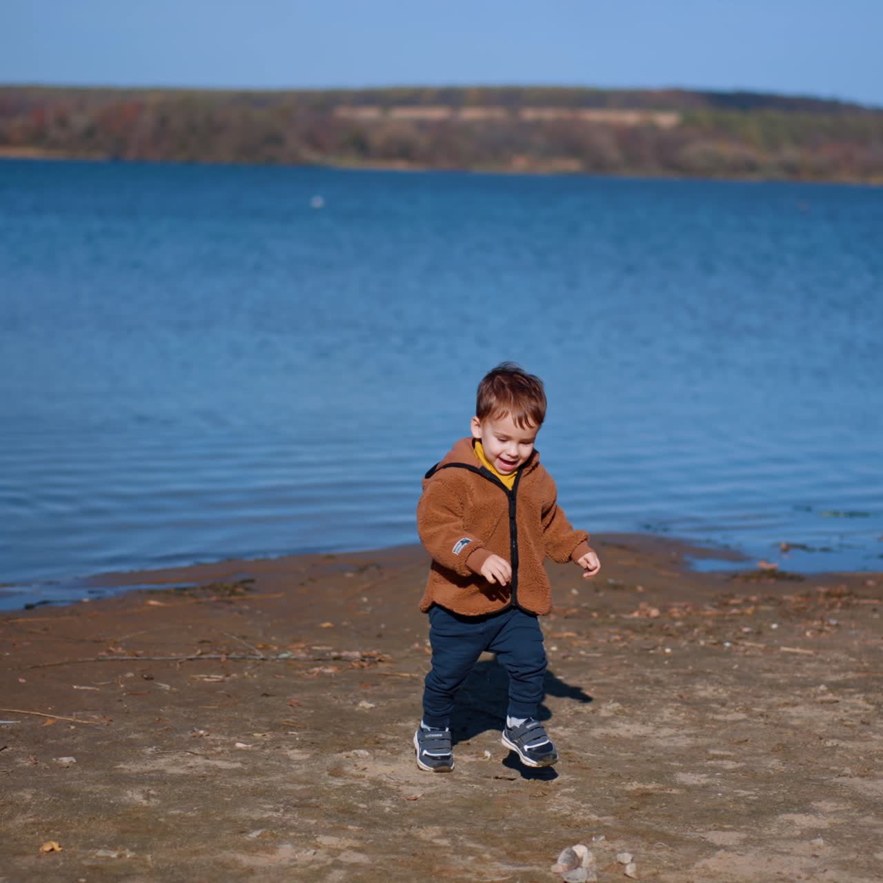Un niño pequeño se divierte tirando piedras al río. El niño coge alegremente otra piedra y la lanza al agua.