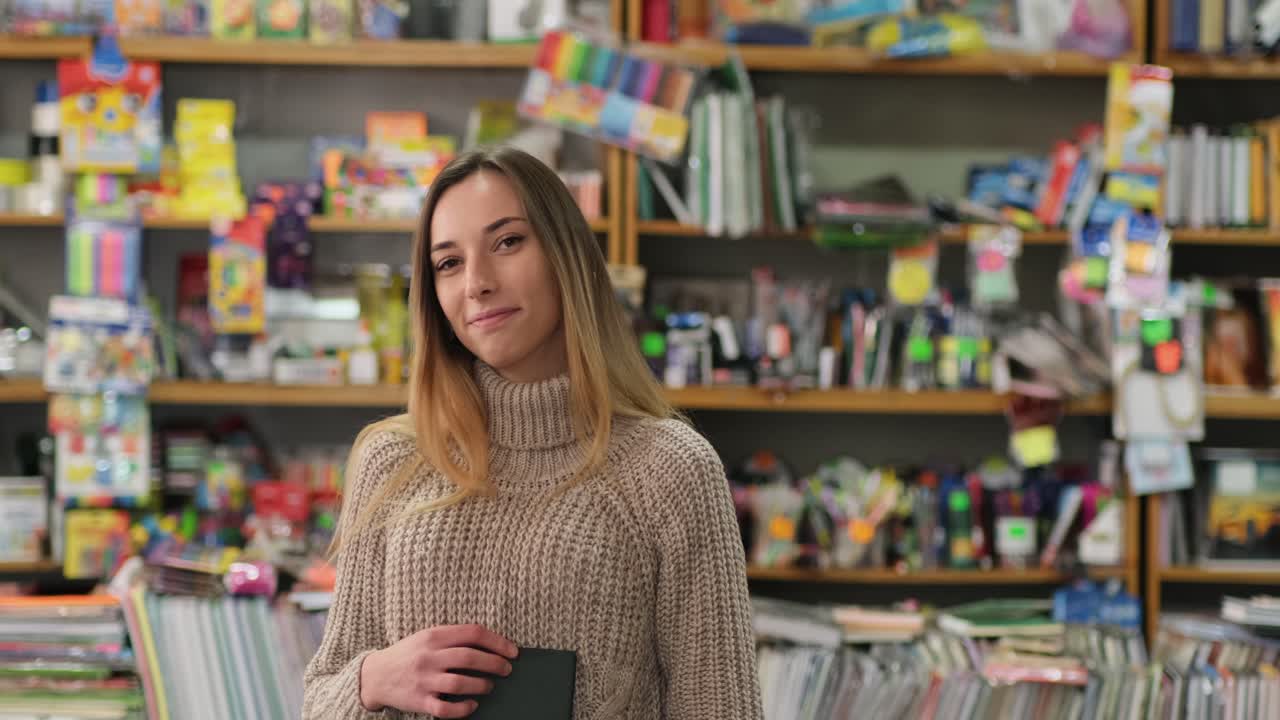 chica inteligente sosteniendo un libro en sus manos en la biblioteca y sonriendo
