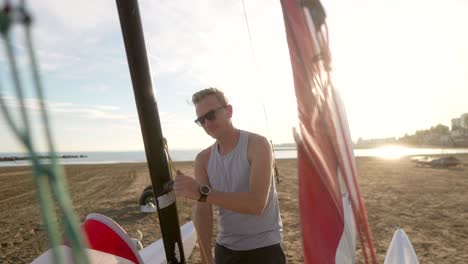 man raising the sail of a hobie cat