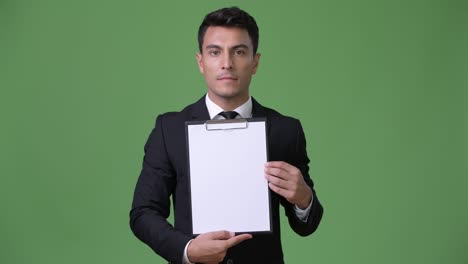 young handsome hispanic businessman against green background