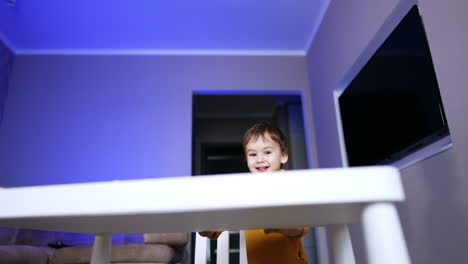 cheerful baby boy playing hide and seek with camera. smiling kid sits down at desk to play puzzles.