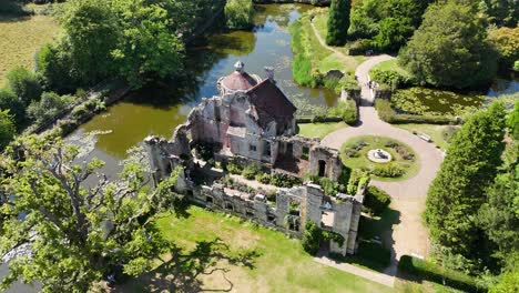 Majestic aerial view of Scotney Castle in Kent, showcasing its medieval ruins surrounded by a picturesque moat, gardens and woodland. Perfect historic stock footage for documentaries and travel
