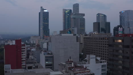 Drone-camera-rising-in-twilight-time.-City-downtown-with-tall-modern-commercial-buildings.-Mexico-city,-Mexico.