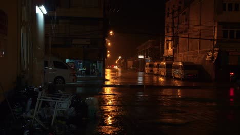 street lights dimly illuminate road on a wet and rainy night as car passes by, thailand