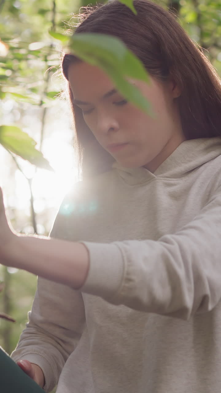 una mujer utiliza una rama de árbol para estirar la pierna levantada en el bosque. una mujer concentrada realiza ejercicios de estiramiento para aliviar la tensión en las piernas después de correr en un día soleado