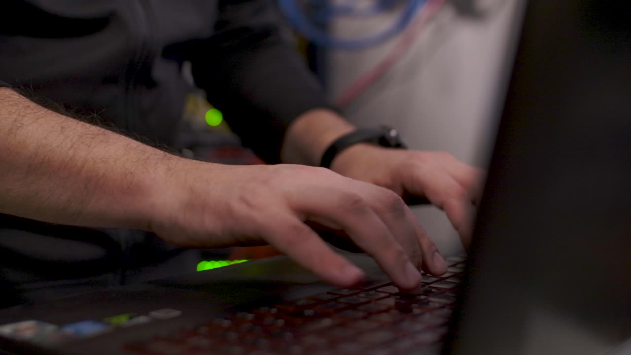 un técnico, dentro de la sala de servidores, abre una computadora portátil y escribe algo