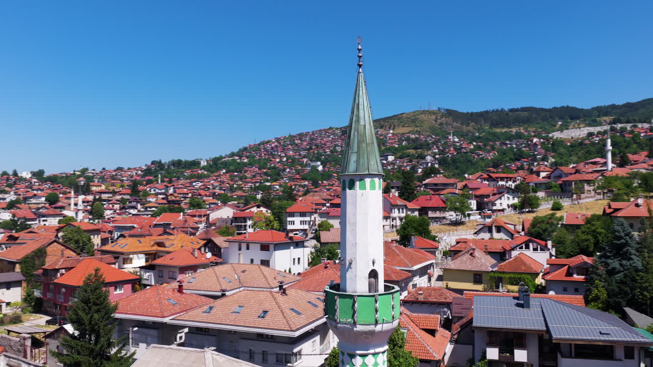 Minaret With Green Top Above Red-roofed Houses In Hillside Neighborhood In Sarajevo, Bosnia and Herzegovina. aerial orbiting shot