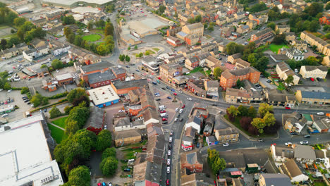 A-drone-records-Heckmondwike,-UK,-with-industrial-buildings,-bustling-streets,-and-the-old-town-center-on-a-summer-evening